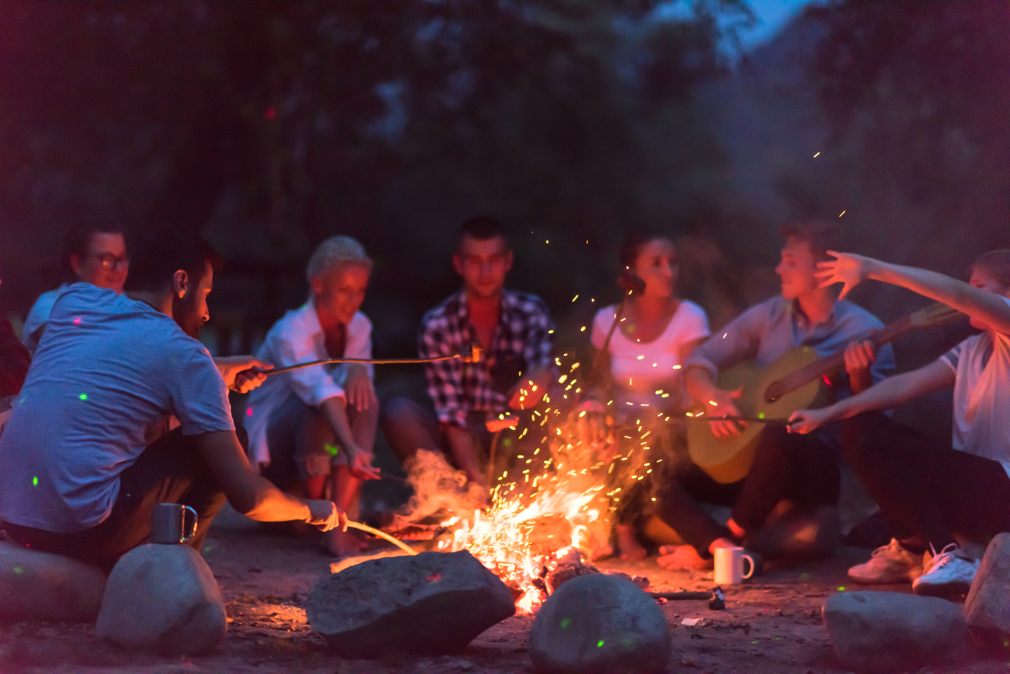 Group of people sitting next to a campfire making music